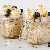 Zwei Gläser mit Overnight Oats, garniert mit Bananenscheiben, Blaubeeren und Granola. Perfekt für ein schnelles Frühstück.