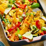 Buntes Gericht mit Reis, Paprika, Zucchini, Karotten und Cashewkernen, garniert mit Koriander und Limettenspalten. Ein köstliches Gericht mit Reis.