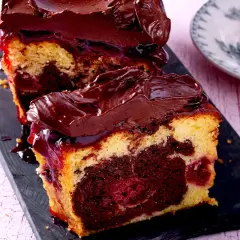 Saftiger Marmorkuchen mit Kirschen und Schokoladenglasur, auf einem dunklen Brett serviert.