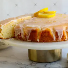 Ein saftiger Zitronenkuchen mit Zuckerguss und Zitronenscheiben, der beste Zitronenkuchen der Welt, wird auf einer Tortenplatte präsentiert.