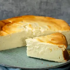 Ein saftiger Quarkkuchen ohne Boden, goldbraun gebacken, liegt auf einem Teller. Ein Stück ist bereits angeschnitten.