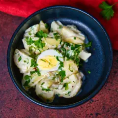 Ein cremiger Kartoffelsalat mit Mayo, garniert mit Petersilie und einem halben Ei. Perfekt für ein Picknick!