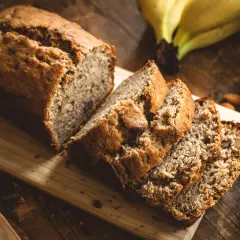 Ein saftiges Bananenbrot, perfekt für ein Bananenbrot Rezept ohne Zucker. Daneben liegen Mandeln und reife Bananen.