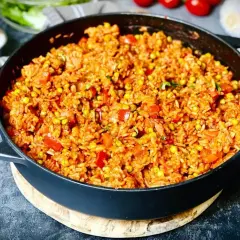 Herzhafter Djuvec Reis mit Mais und Paprika, serviert in einer Gusseisenpfanne. Ein köstliches Gericht, das nach mehr schmeckt.