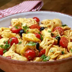 Herzhafter Tortellini Salat mit Kirschtomaten, schwarzen Oliven und frischem Basilikum in einer rustikalen Schüssel.