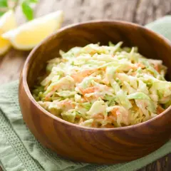 Cremiger Krautsalat mit Karotten, perfekt für jedes BBQ. Ein einfaches coleslaw rezept, das immer gelingt. Serviert in einer Holzschale mit Zitronenspalten.