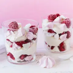 Zwei Gläser mit Himbeer Baiser Dessert, geschichtet mit Sahne, frischen Himbeeren und zarten Baiserstückchen.