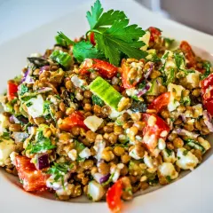Ein bunter Linsensalat mit Feta, Gurken, Tomaten und roten Zwiebeln, garniert mit Petersilie.