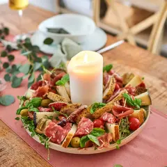 Eine festliche Platte mit Wurst, Käse, Brot und Oliven, die zum Antipasti selber machen einlädt. Ein Kerzenlicht sorgt für Gemütlichkeit.