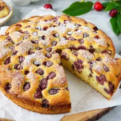 Saftiger kuchen mit kirschen, bestäubt mit Puderzucker. Ein Stück wurde bereits herausgeschnitten.
