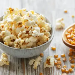 Schüssel mit frisch gemachtem Popcorn, daneben Maiskörner in einem Holzlöffel. So einfach ist Popcorn selber machen!