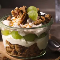 Ein köstliches Dessert im Glas: Schichten aus cremigem Joghurt, saftigen Weintrauben und knusprigen Cookie-Stücken, garniert mit Pekannüssen.