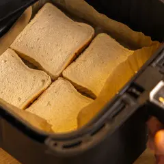 Vier Scheiben Toastbrot liegen in der Schublade eines Airfryers, bereit für ein schnelles Toast Hawaii.