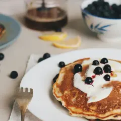 Leckere Pfannkuchen ohne Ei, garniert mit Joghurt und Blaubeeren, serviert mit Honig und Zitronenspalten.