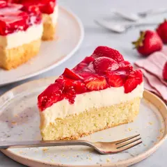 Ein saftiges Stück Erdbeer Schmand Kuchen mit frischen Erdbeeren und Tortenguss auf einem Teller, daneben frische Erdbeeren und eine Gabel.