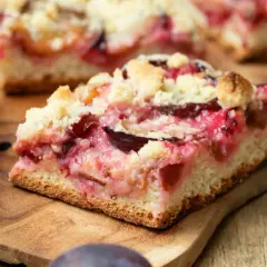 Saftiger Zwetschgenkuchen mit Streuseln auf einem Holzbrett. Ein Stück ist angeschnitten und zeigt die saftigen Früchte.