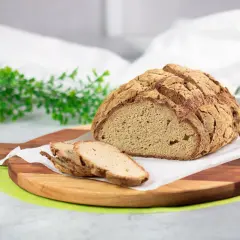Ein rustikales Brot ohne Kohlenhydrate, aufgeschnitten auf einem Holzbrett, mit grünen Zweigen und Lavendel im Hintergrund.