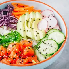 Bunte Poke Bowl mit Lachs, Avocado, Edamame, Gurke, Radieschen, Rotkohl und Seetang auf Reis.