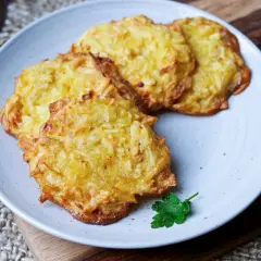Goldbraune Kartoffelpuffer im Airfryer, knusprig und lecker, auf einem Teller mit Petersilie garniert.