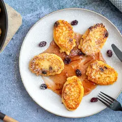 Goldbraune Quarkkeulchen ohne Kartoffeln, mit Puderzucker bestäubt und mit Rosinen garniert, serviert mit fruchtiger Soße.