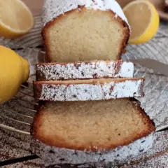 Zitronenkuchen wie bei Oma, mit Puderzucker bestäubt, neben frischen Zitronen auf einem Gitterrost.
