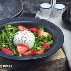Ein frischer Spargelsalat mit Erdbeeren und Burrata, garniert mit Kräutern und Pfeffer.