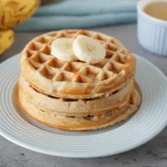 Stapel goldbrauner bananenwaffeln ohne zucker, garniert mit Bananenscheiben. Daneben liegen reife Bananen.