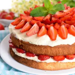 Eine zweistöckige Erdbeer-Sahne-Torte, üppig belegt mit frischen Erdbeerscheiben und garniert mit Minze.