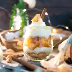 Leckeres Apfel-Crumble-Dessert im Glas mit Zimtstange und Sahne. Ein süßer Genuss, der zum Naschen einlädt.