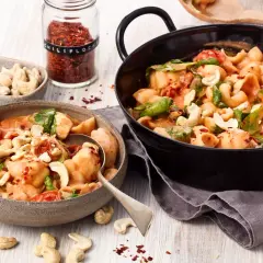 Ausgefallene Pasta-Rezepte vegetarisch: Cremige Muschelnudeln mit Cashews, Tomaten und Spinat, bestreut mit Chili-Flocken.