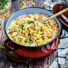 Herzhaftes Nudelgericht mit Würstchen, Erbsen und Hähnchen in cremiger Sauce. Köstliche gerichte mit sahne, garniert mit Petersilie.