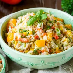 Erfrischender Reissalat mit Mandarinen, Paprika, Mais und Kräutern, garniert mit Basilikum.