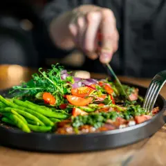 Ein Teller mit frischem Gemüse, wie grüne Bohnen und Tomaten, inspiriert von clean eating rezepten. Eine Person schneidet das Essen mit Messer und Gabel.