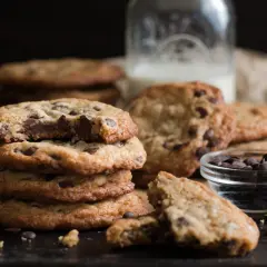 Ein Stapel saftiger Chocolate Chip Cookies, perfekt für ein einfaches Cookies Rezept. Daneben eine Schale Schokodrops und ein Glas Milch.