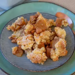 Ein Teller mit warmem Apfel Crumble, bestäubt mit Puderzucker. Die goldbraunen Apfelstücke und knusprigen Streusel laden zum Genießen ein.