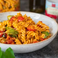 Ein köstlicher Nudelsalat mit Pesto, Kirschtomaten und frischem Basilikum in einer Schüssel.