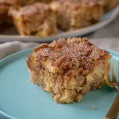 Ein Stück saftiger Apfel Zimt Kuchen mit knuspriger Kruste auf einem türkisfarbenen Teller, daneben zwei goldene Gabeln.