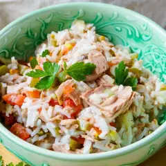 Reissalat mit Thunfisch, Tomaten und Gurken, garniert mit Petersilie, in einer grünen Schüssel.