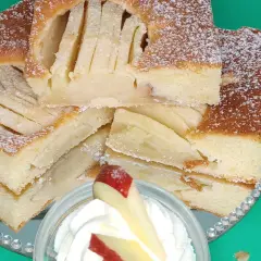 Saftiger Apfelkuchen vom Blech, mit Puderzucker bestäubt und auf einem Spiegel serviert. Ein Stück mit Sahne und Apfel garniert.