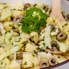 Ein köstlicher Kartoffelsalat ohne Mayo mit Gurken, Oliven und Kapern, garniert mit Petersilie.