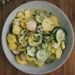 Bayrischer Kartoffelsalat mit Speck und Zwiebeln, garniert mit Radieschen, Gurken und Schnittlauch. Ein deftiger Genuss!