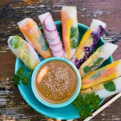 Frische Sommerrollen mit bunten Gemüsesorten, garniert mit Sesam, serviert mit Erdnussdip. Perfekt für ein leichtes Sommerrollen Rezept.