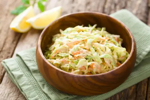 Cremiger Krautsalat mit Karotten, perfekt für jedes BBQ. Ein einfaches coleslaw rezept, das immer gelingt. Serviert in einer Holzschale mit Zitronenspalten.