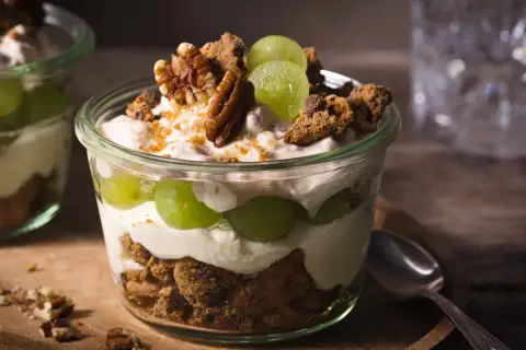 Ein köstliches Dessert im Glas: Schichten aus cremigem Joghurt, saftigen Weintrauben und knusprigen Cookie-Stücken, garniert mit Pekannüssen.