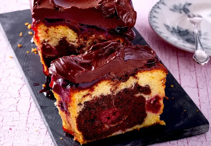 Saftiger Marmorkuchen mit Kirschen und Schokoladenglasur, auf einem dunklen Brett serviert.