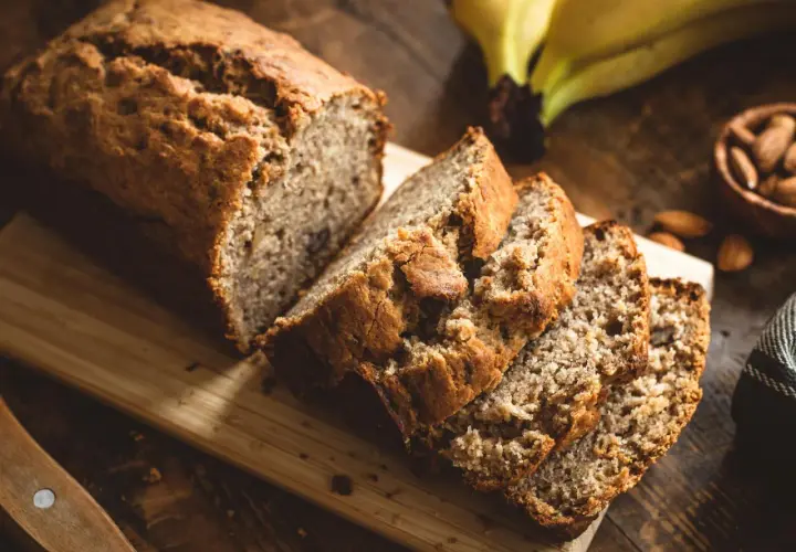 Ein saftiges Bananenbrot, perfekt für ein Bananenbrot Rezept ohne Zucker. Daneben liegen Mandeln und reife Bananen.