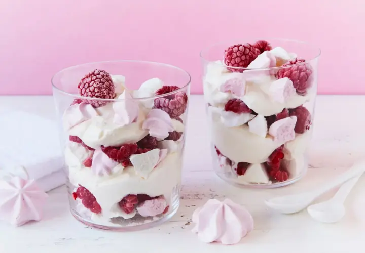 Zwei Gläser mit Himbeer Baiser Dessert, geschichtet mit Sahne, frischen Himbeeren und zarten Baiserstückchen.