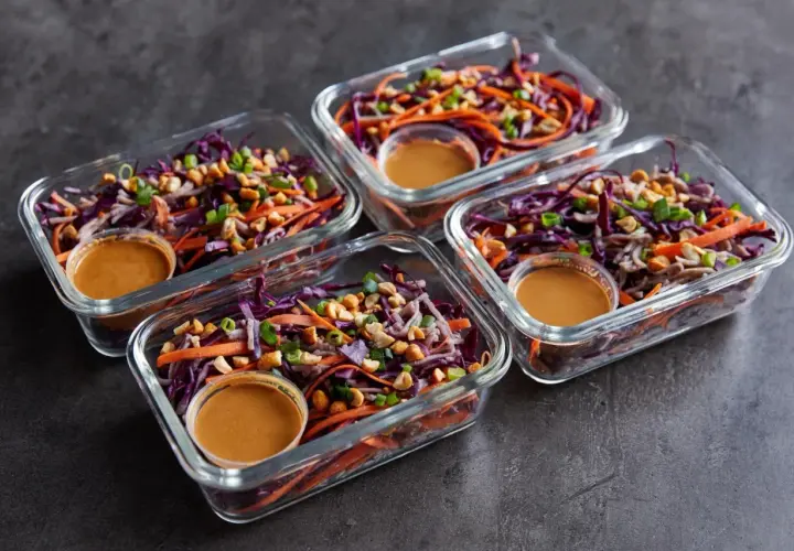 Vier Glasbehälter mit einem bunten Salat aus Rotkohl, Karotten und Erdnüssen. Perfekt für Rezepte mit viel Protein und wenig Kalorien.