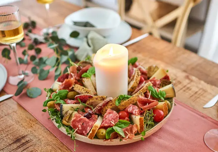 Eine festliche Platte mit Wurst, Käse, Brot und Oliven, die zum Antipasti selber machen einlädt. Ein Kerzenlicht sorgt für Gemütlichkeit.