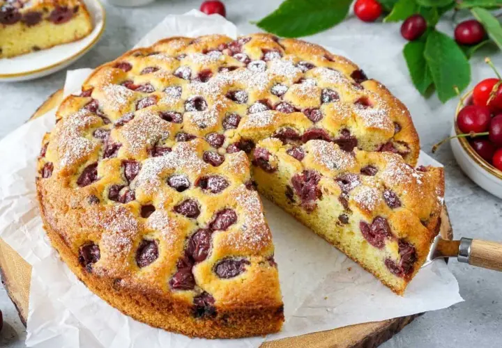 Saftiger kuchen mit kirschen, bestäubt mit Puderzucker. Ein Stück wurde bereits herausgeschnitten.